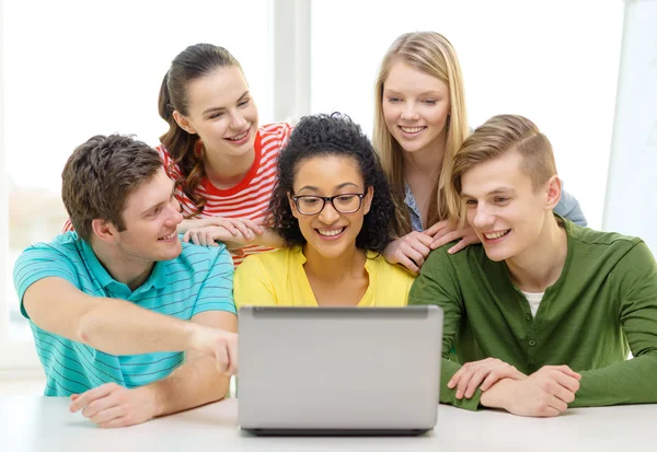 Lachende studenten kijken naar laptop op school — Stockfoto