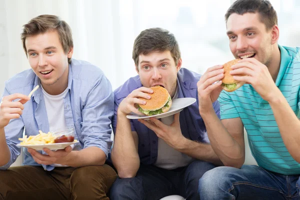 Amigos sonrientes con refrescos y hamburguesas en casa —  Fotos de Stock