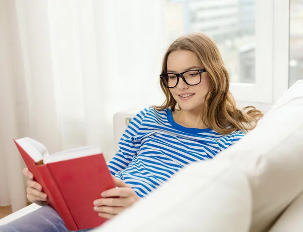 Улыбающаяся девочка-подросток читает книгу на диване — стоковое фото