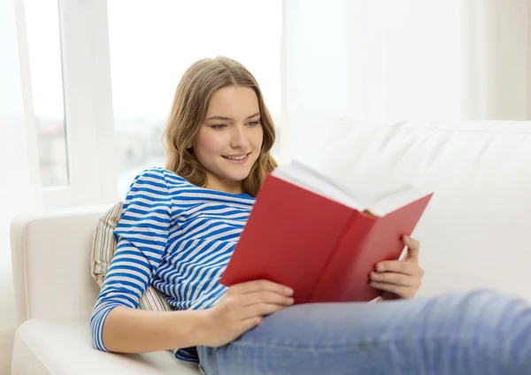 Smiling teenage girl reading book on couch — Stock Photo, Image