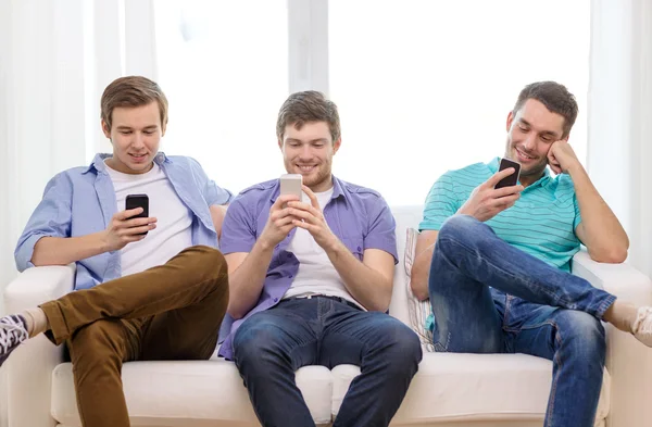 Amigos sonrientes con teléfonos inteligentes en casa —  Fotos de Stock