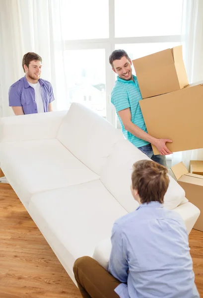 Amigos sonrientes con sofá y cajas en casa nueva —  Fotos de Stock