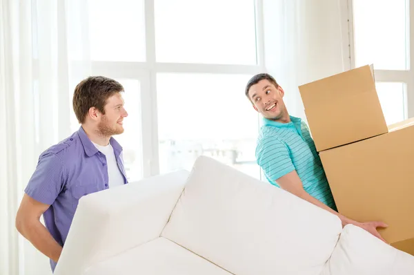 Amigos sonrientes con sofá y cajas en casa nueva —  Fotos de Stock