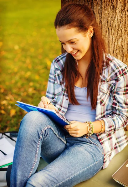 Adolescente sorridente escrevendo em caderno — Fotografia de Stock