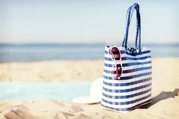 Strohhut, Sonnenbrille und Tasche liegen im Sand — Stockfoto