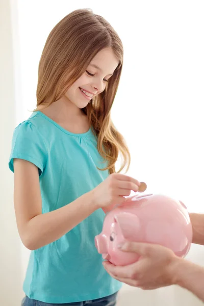 Lächelndes kleines Mädchen steckt Münze in Sparschwein — Stockfoto
