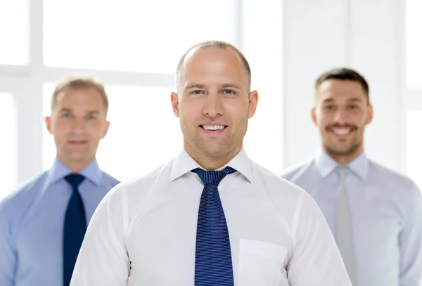 Empresário sorridente no cargo com equipe nas costas — Fotografia de Stock