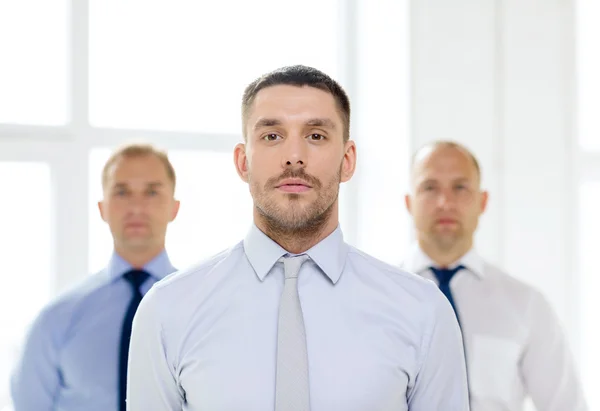 Poważny biznesmen w biurze z zespołem na plecach — Stockfoto