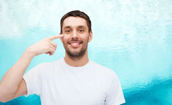 Smiling young handsome man pointing to eyes — Stock Photo, Image