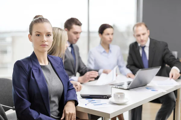 Businesswoman in office with team on the back — Stock Photo, Image