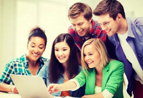 Lachende studenten kijken naar laptop op school — Stockfoto