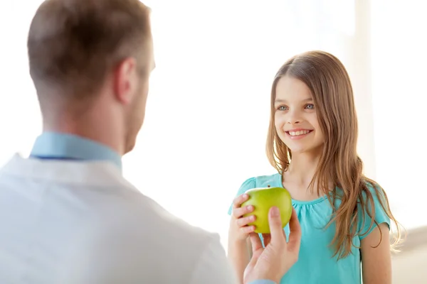 Arzt schenkt lächelndem kleinen Mädchen einen Apfel — Stockfoto