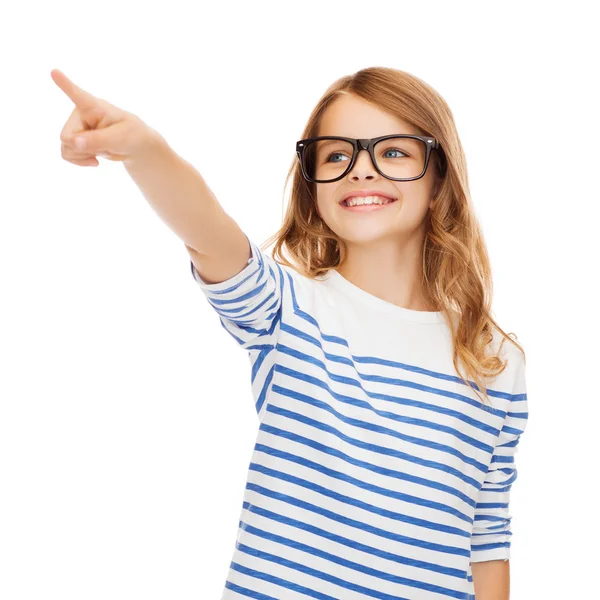 Cute little girl in eyeglasses pointing in the air — Stock Photo, Image