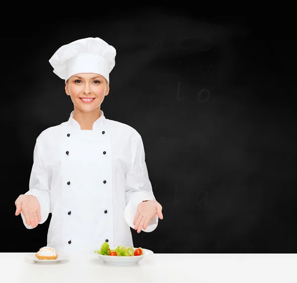 Lachende vrouwelijke chef-kok met salade en taart op platen — Stockfoto