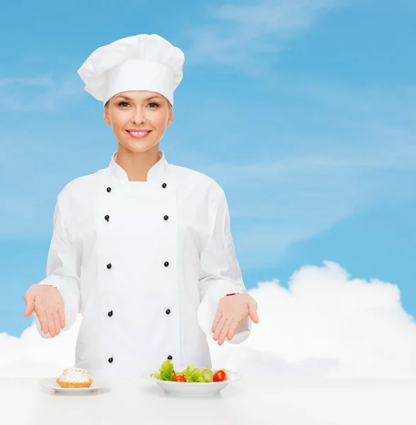 Lachende vrouwelijke chef-kok met salade en taart op platen — Stockfoto