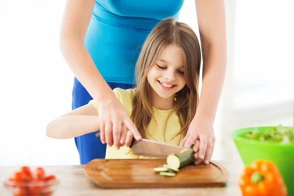 Niña sonriente con madre cortando pepino — Foto de Stock