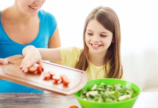 Menina com a mãe adicionando tomates à salada — Fotografia de Stock