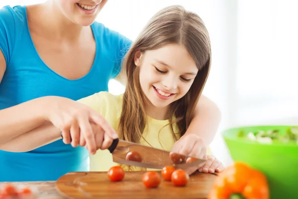 Petite fille souriante avec mère hachant des tomates — Photo