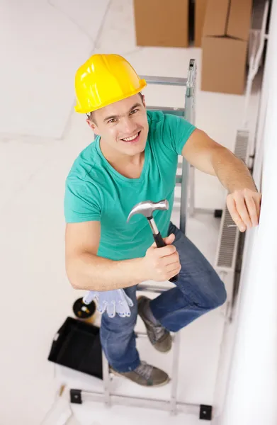 Sorrindo homem no capacete martelando prego na parede — Fotografia de Stock