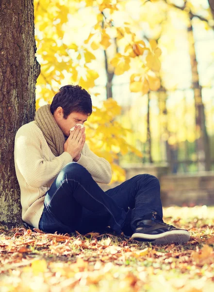 Ill man with paper tissue in autumn park — Stock Photo, Image