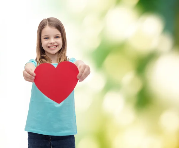 Kırmızı kalp veren küçük kız gülümseyerek — Stok fotoğraf