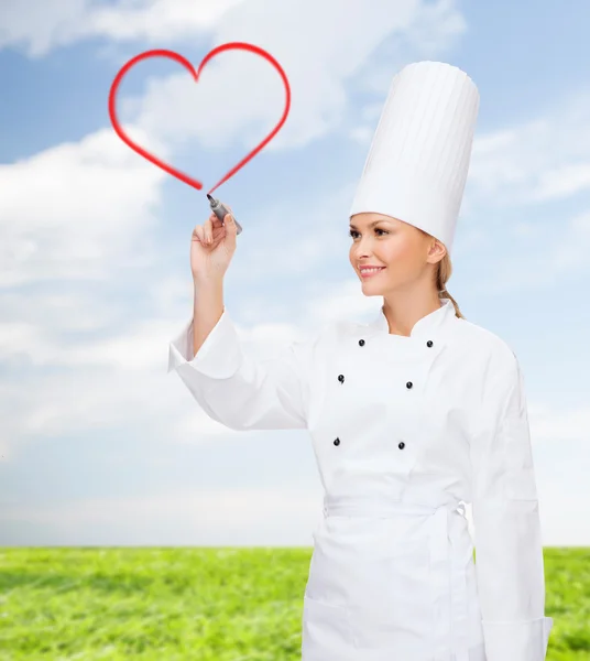Улыбающаяся женщина шеф-повар рисует красное сердце в воздухе — стоковое фото
