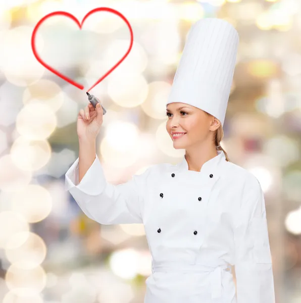 Glimlachend vrouwelijke chef-kok tekening rood hart op lucht — Stockfoto