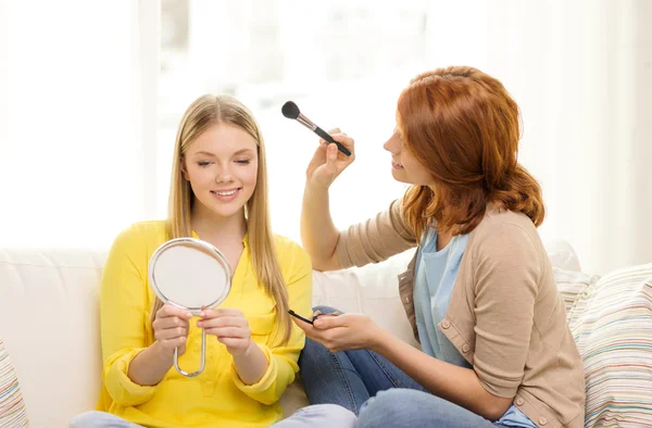 Dos niñas adolescentes sonrientes aplicando maquillaje en casa Fotos De Stock Sin Royalties Gratis