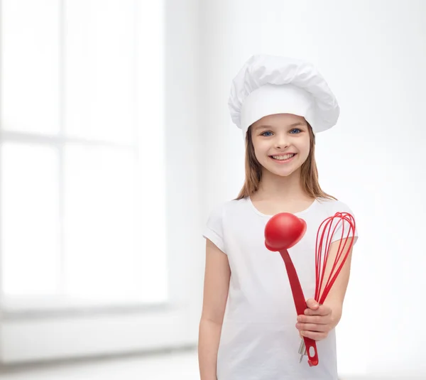 Fille souriante dans chapeau de cuisine avec louche et fouet — Photo