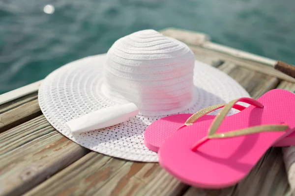Close up of hat, sunscreen and slippers at seaside — Stock Photo, Image