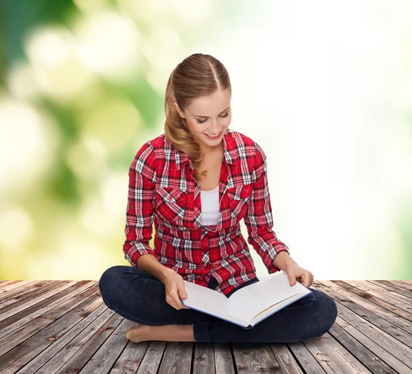 Jeune femme souriante assise sur le sol avec un livre — Photo