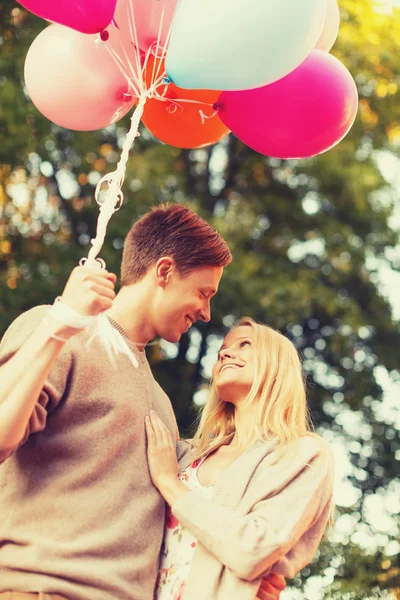 Casal sorridente com balões coloridos no parque — Fotografia de Stock