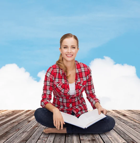 Jeune femme souriante assise sur le sol avec un livre — Photo