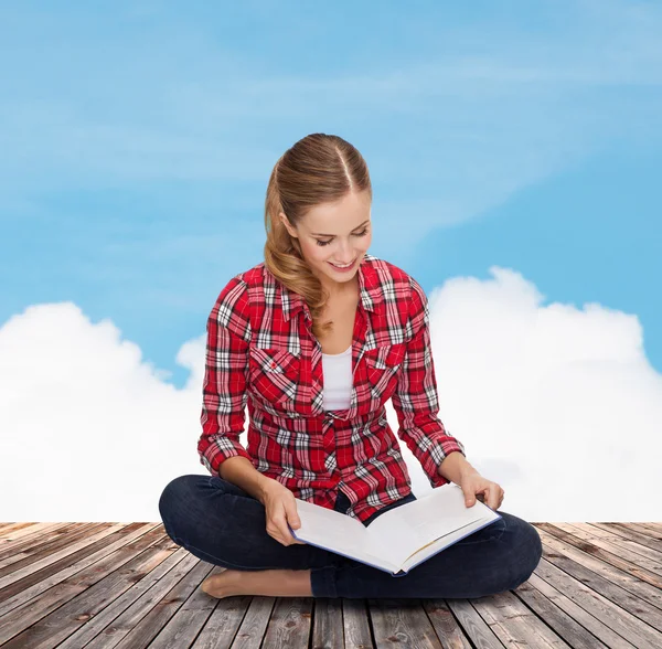 Jeune femme souriante assise sur le sol avec un livre — Photo