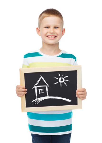 Smiling little boy holding chalkboard with home — Stock Photo, Image