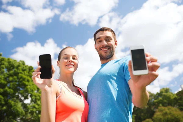 Due persone sorridenti con smartphone all'aperto — Foto Stock