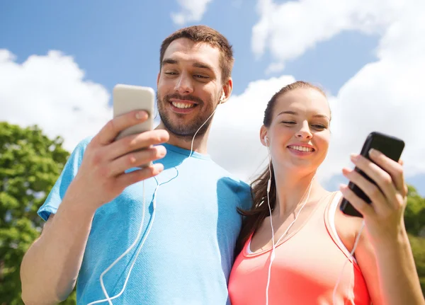 Два улыбающихся человека со смартфонами на улице — стоковое фото