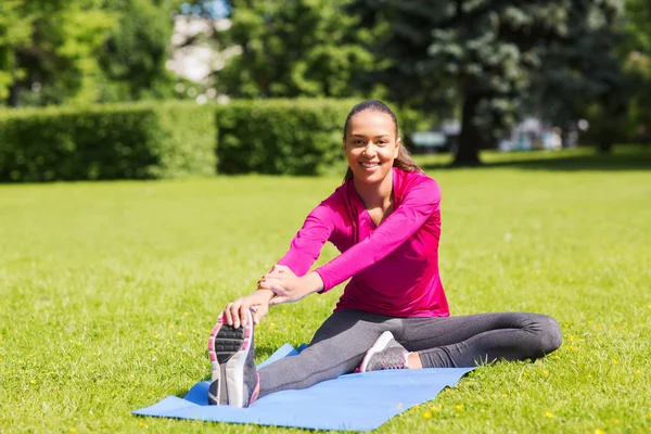 Lächelnde Frau streckt Bein auf Matte im Freien — Stockfoto