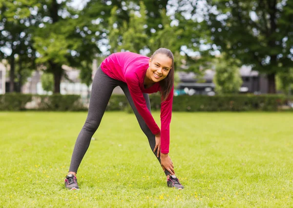 Sonriente negro mujer estirando la pierna al aire libre — Foto de Stock