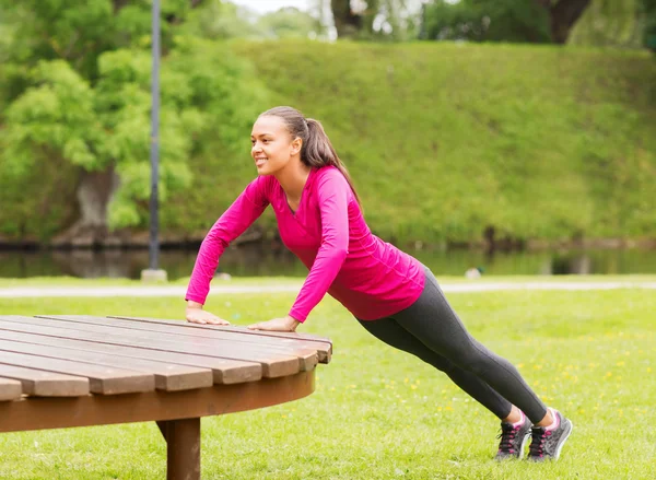 Smiling woman doing push-ups on bench outdoors — Stock Photo, Image