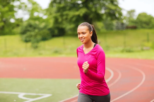 Souriant jeune femme courir sur la piste à l'extérieur — Photo