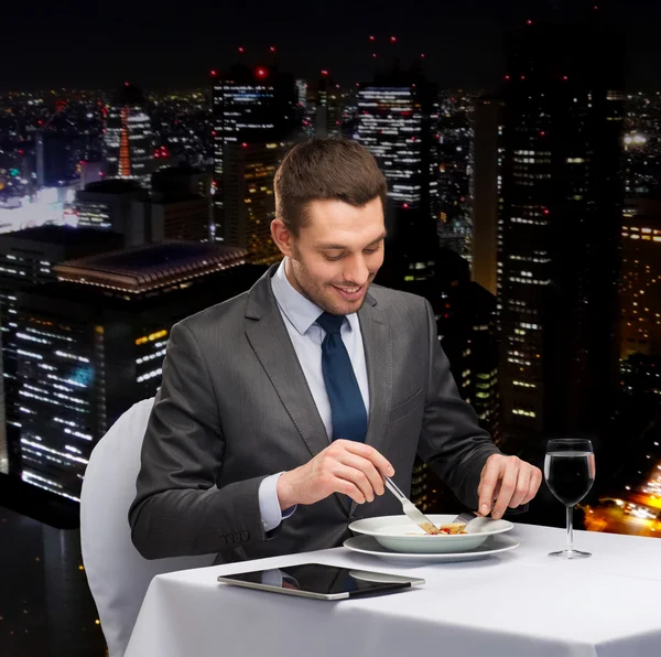 Smiling man with tablet pc eating main course — Stock Photo, Image