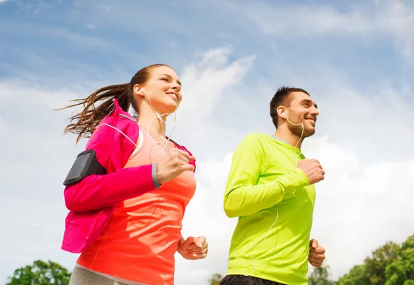 Sonriente pareja con auriculares corriendo al aire libre — Foto de Stock