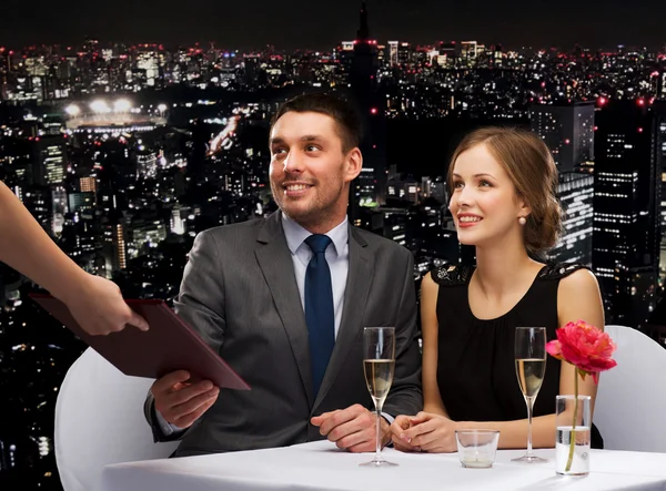 Waiter giving menu to happy couple at restaurant — Stock Photo, Image