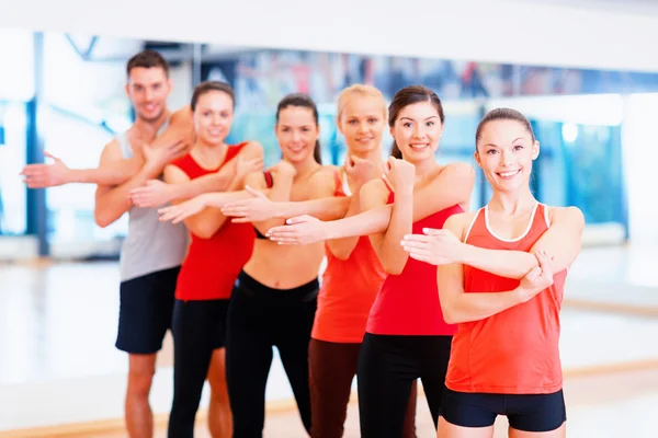 Grupo de personas sonrientes estirándose en el gimnasio — Foto de Stock