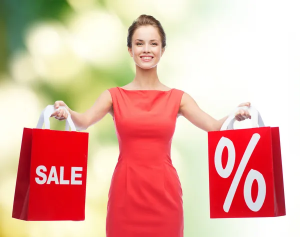 Ung kvinna i röd klänning med shoppingväskor — Stockfoto