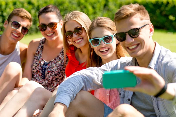Amigos sonrientes con teléfono inteligente sentado en la hierba —  Fotos de Stock