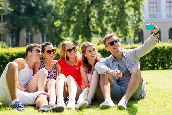 Улыбающиеся друзья со смартфоном, сидящие на траве — стоковое фото