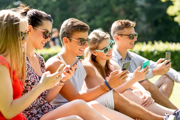 Amigos sonrientes con teléfonos inteligentes sentados en la hierba —  Fotos de Stock