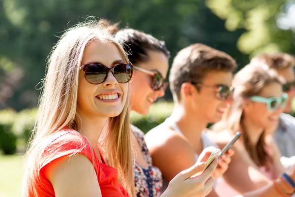 Lachende vrienden met smartphones zitten in park — Stockfoto
